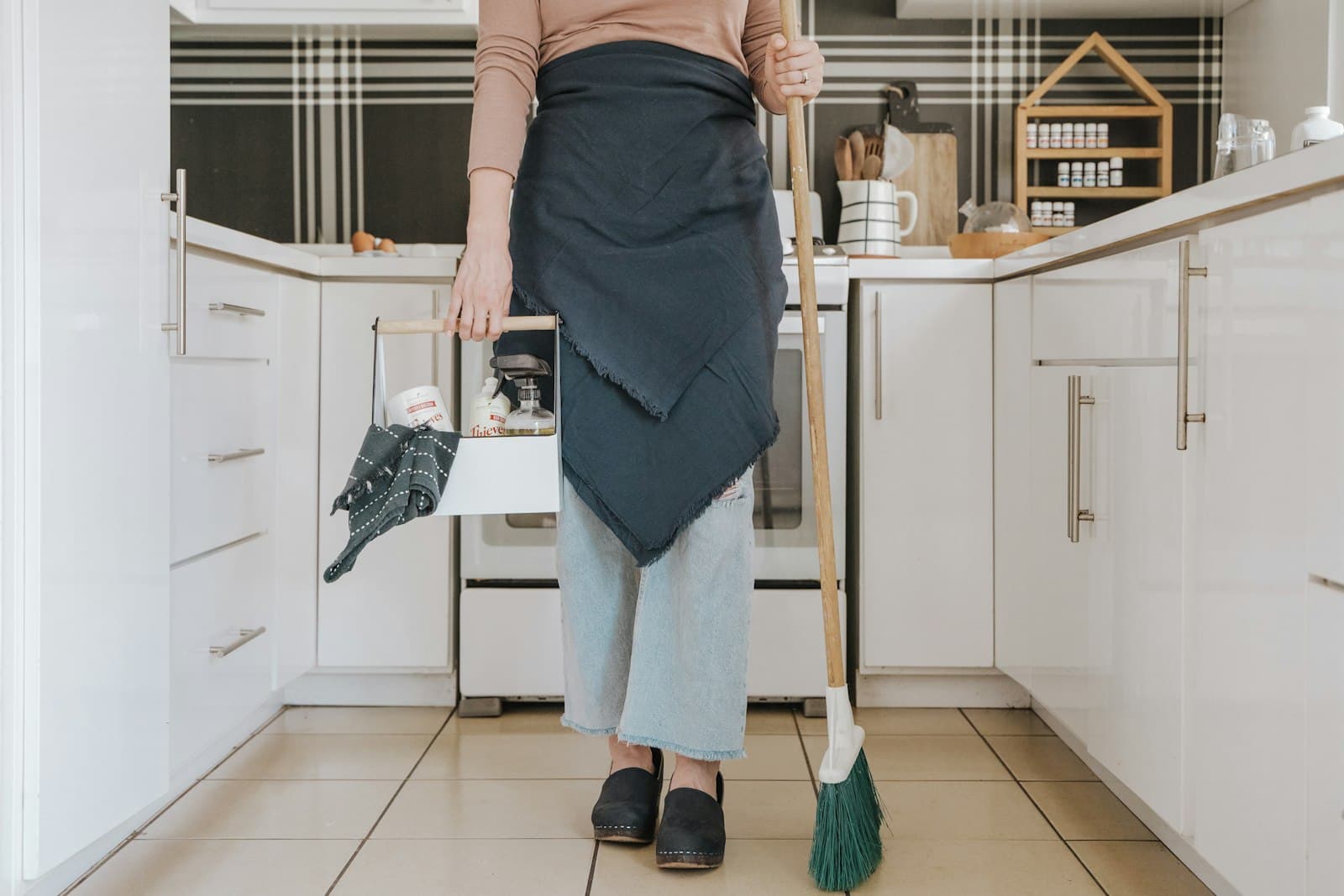 Trabalhadora de uniforme com uma vassoura, em uma cozinha profissional